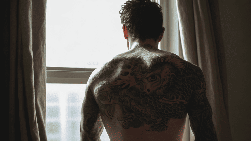 man heeft een tattoo op zijn rug en kijk uit het raam