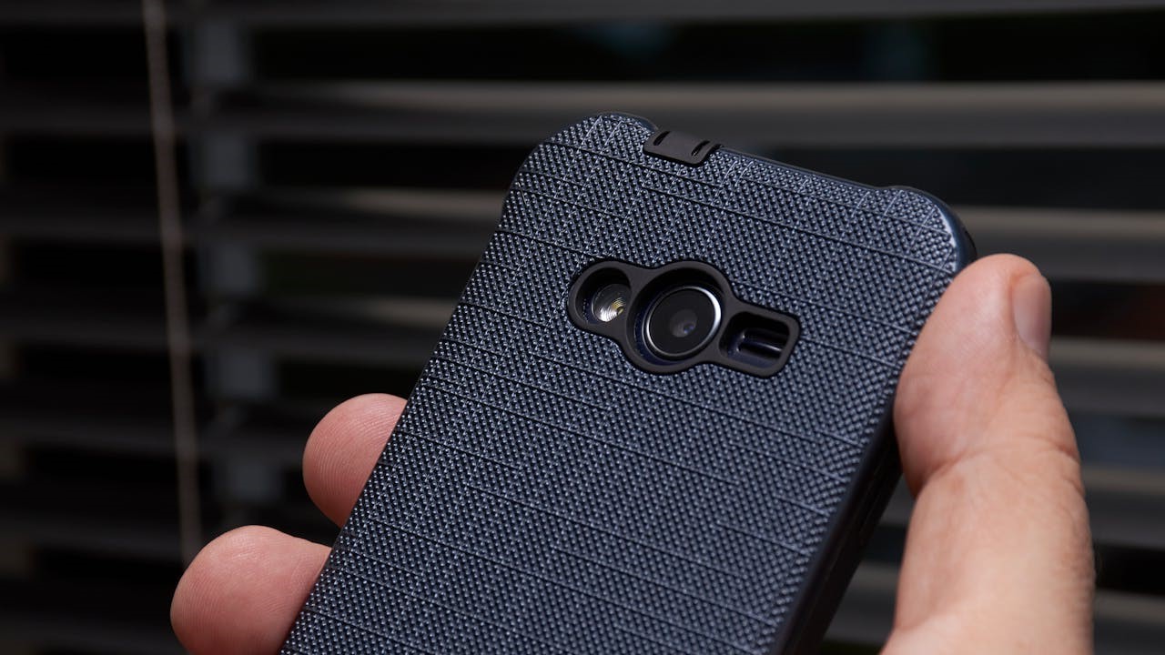 Close-up van een hand die een smartphone met donkergrijze, gestructureerde hoes vasthoudt – telefoon personaliseren.