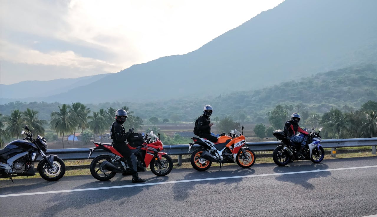 Groep motorrijders in zwarte outfits, staand langs de weg met verschillende sportmotoren, met een berglandschap op de achtergrond