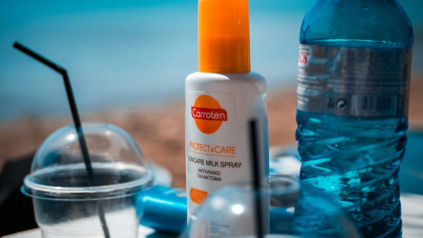 Fles zonnebrand SPF 50 spray op tafel met waterfles en drankje bij zonnige strandsetting