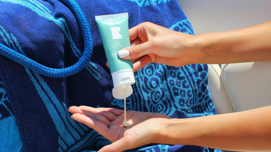 Zonnebrand SPF 50 wordt in de hand geknepen naast strandtas en handdoek in de zon