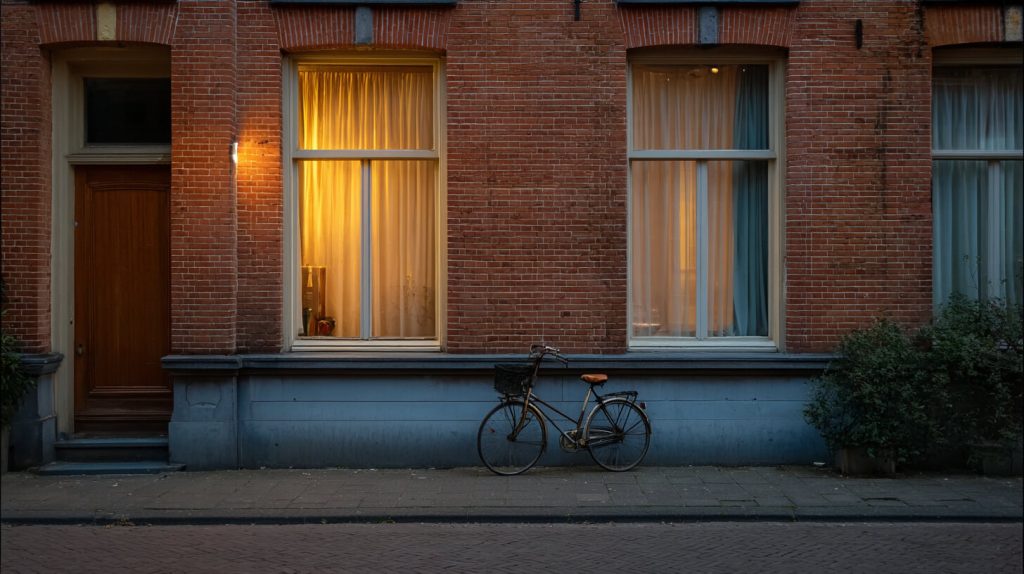 Verlicht raam met gordijnen in een bakstenen gevel met een fiets ervoor, waardoor de woning bewoond oogt